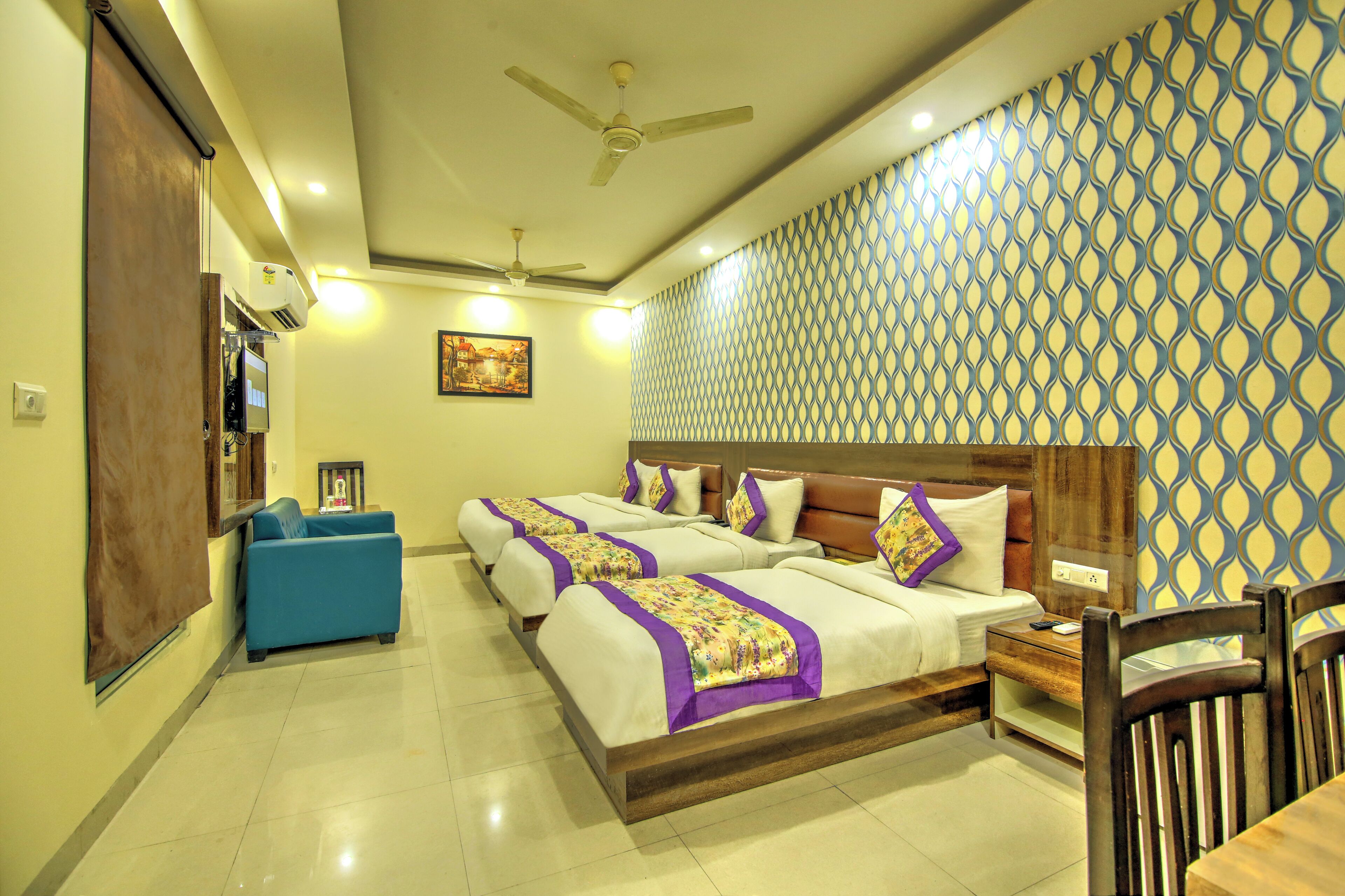 A hotel room with a large bed, a blue sofa, a wooden nightstand, and a ceiling fan.