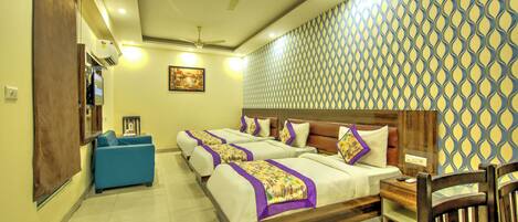A hotel room with a large bed, a blue sofa, a wooden nightstand, and a ceiling fan.