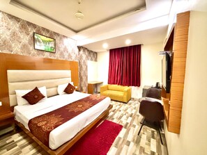 A hotel room with a large bed, a sofa, a desk, and a TV. - Hotel Smart Plaza (New Delhi)