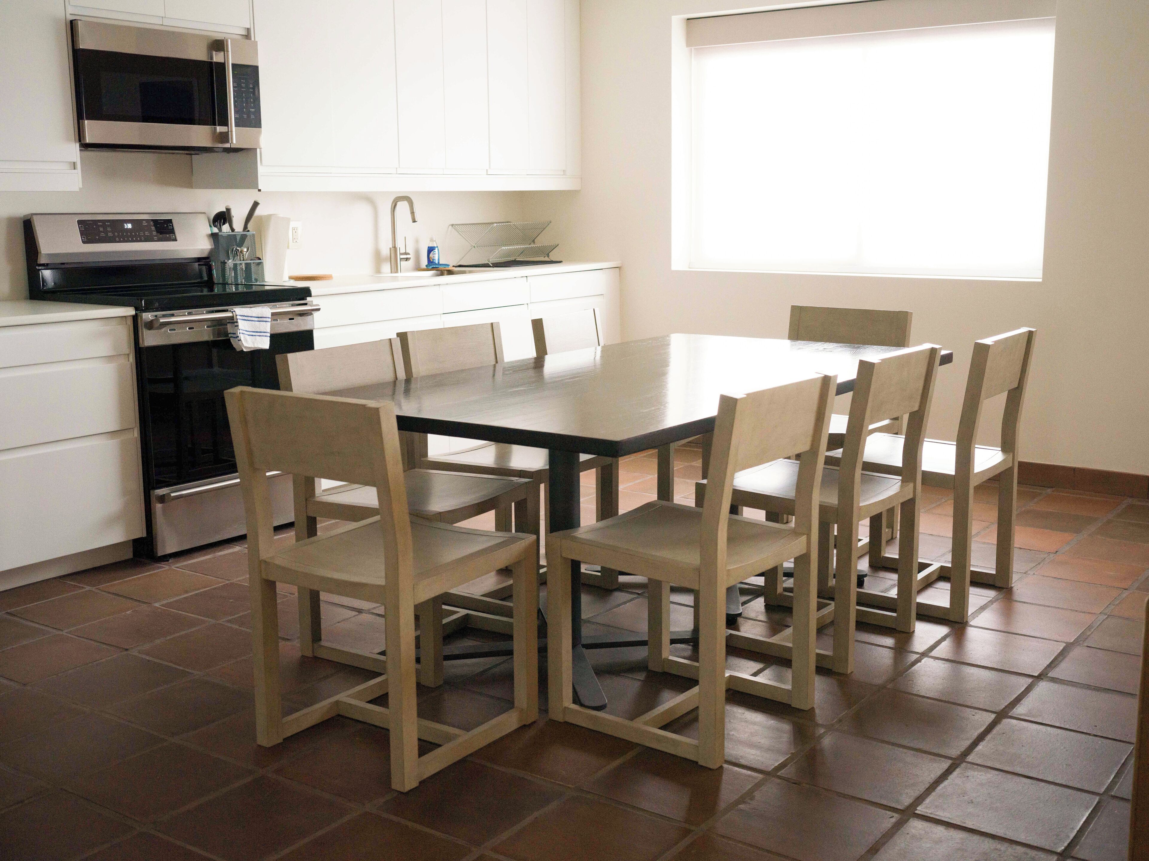 A kitchen with white cabinets, a stainless steel microwave, an oven, and a dining table with six chairs.