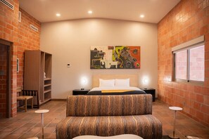 Un dormitorio con cama, mesita de noche, silla, una pequeña mesa y ventana.