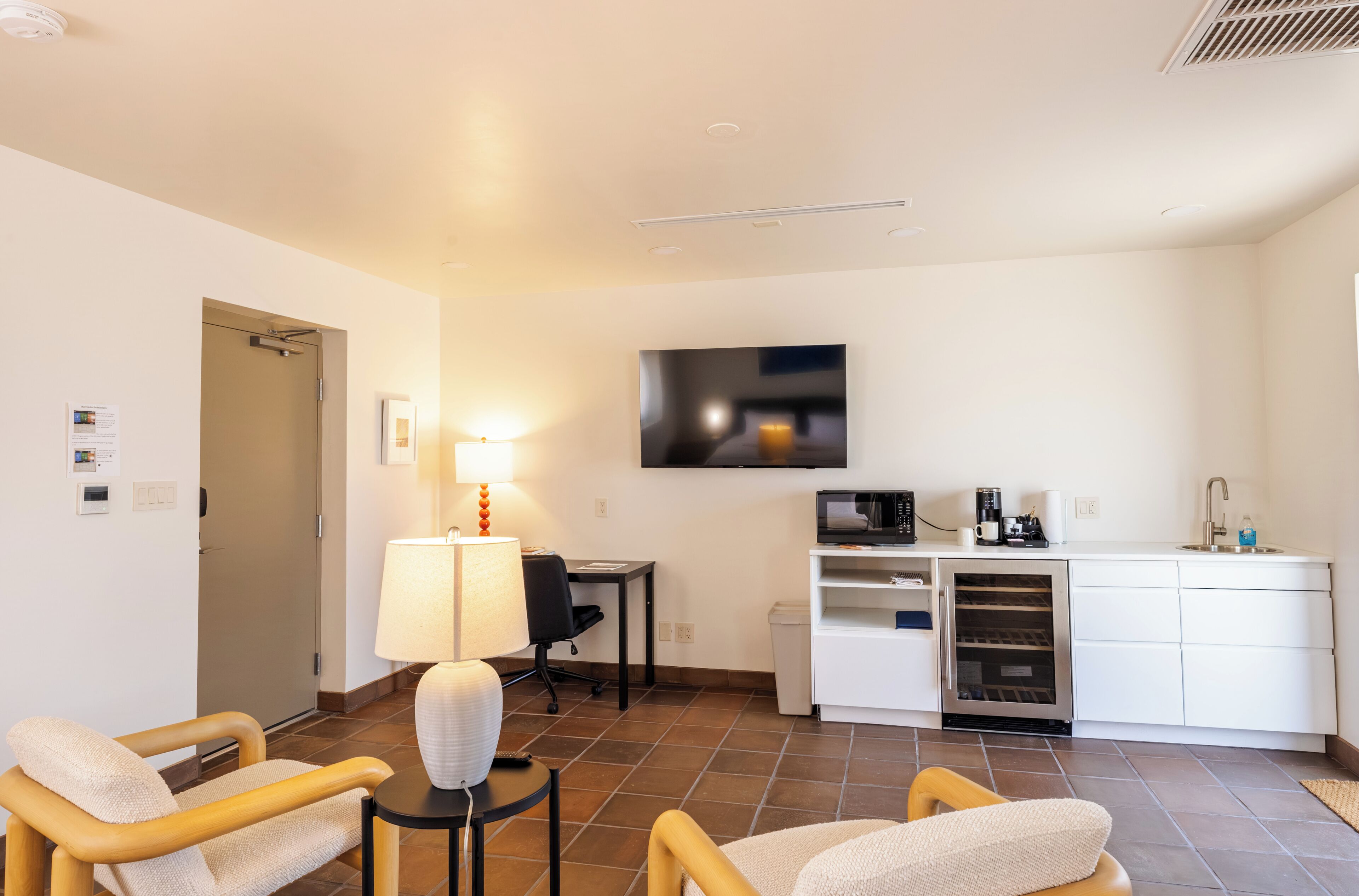 A compact hotel room with a kitchenette, a flat-screen TV, a desk, and two chairs.