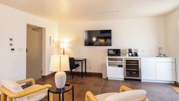 A compact hotel room with a kitchenette, a flat-screen TV, a desk, and two chairs.
