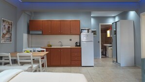 A modern kitchen with wooden cabinets, a white refrigerator, and a dining area with a table and chairs. - Stay & Smile apartments (Kallithea)