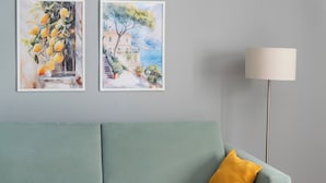 A room with a green sofa, a yellow pillow, and two framed paintings on the wall. - Stay & Smile apartments (Kallithea)