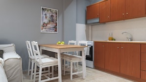A small kitchen with wooden cabinets, a white countertop, and a dining area with a table and chairs. - Stay & Smile apartments (Kallithea)