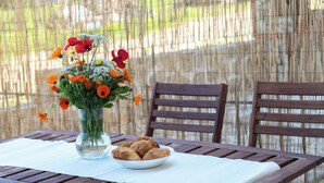 A wooden table with a white tablecloth, a clear glass vase with orange and red flowers, and a bowl of cookies. - Stay & Smile apartments (Kallithea)