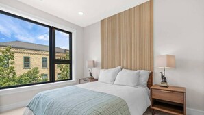 Un dormitorio con un ventanal grande, una cama, dos mesitas de noche con lámparas y un panel de pared de madera.