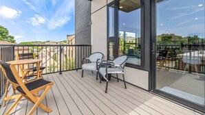 Una terraza de madera con mobiliario exterior, ventanas amplias y vistas del entorno.