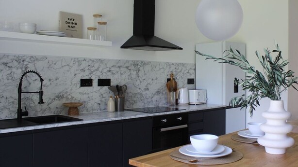 Una cocina moderna con salpicadero de mármol, armarios negros y una mesa de comedor de madera.