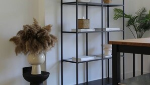 Una estantería de metal negro con un jarrón blanco y una planta en maceta en el estante superior.