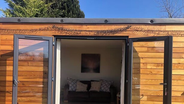 Eine moderne Blockhütte mit Schiebetür zu einem gemütlichen Innenraum mit Sofa und Teppich.
