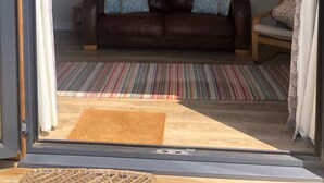 Ein Wohnzimmer mit einem braunen Ledersofa, zwei gemusterten Zierkissen, einem farbenfrohen Streifen Teppich und einer braunen Fußmatte.