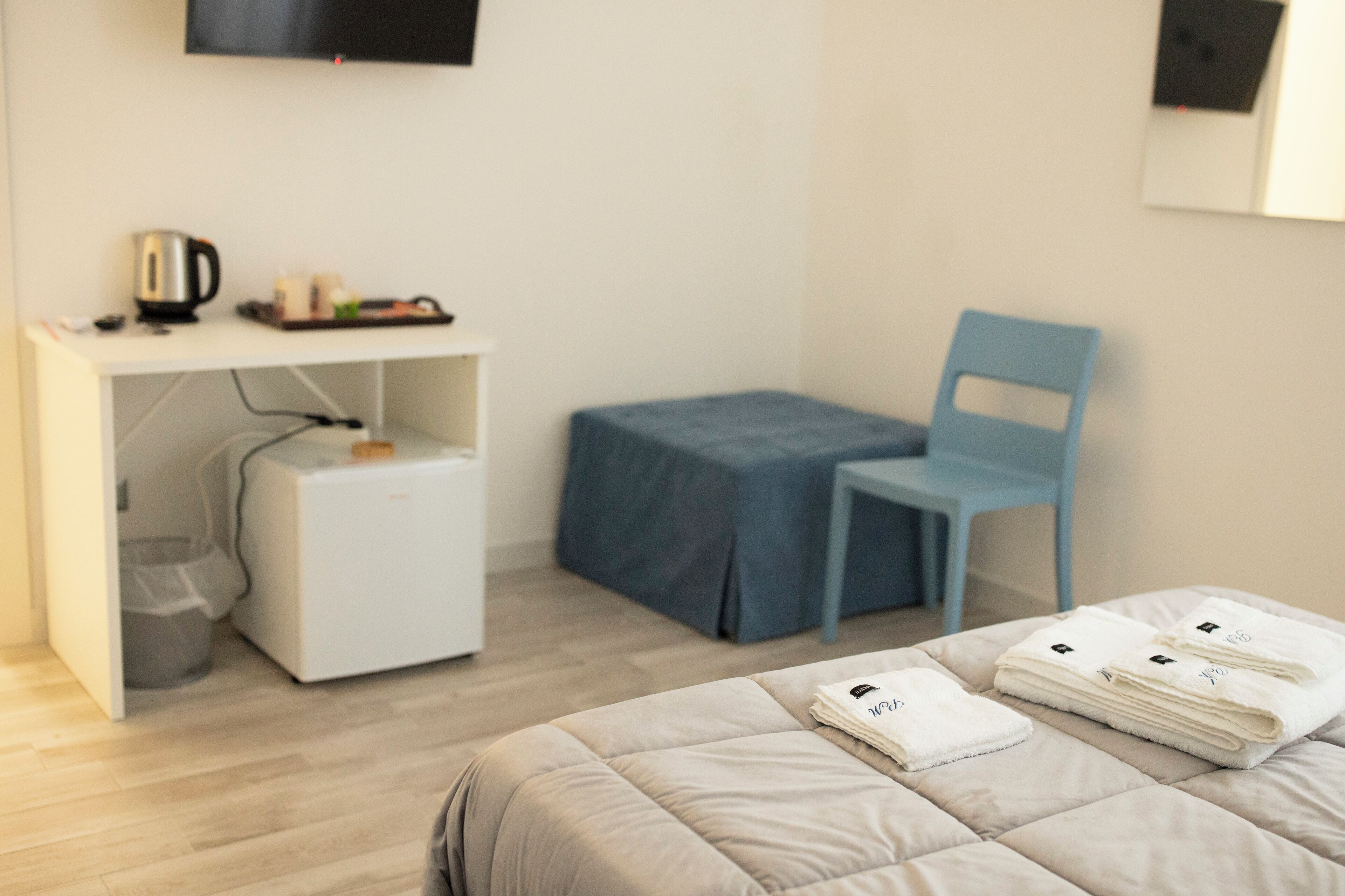 A modern hotel room with a bed, a desk, a chair, and a small kitchenette.