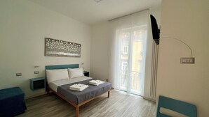 Un dormitorio con cama, mesitas de noche, televisor en la pared y ventana con cortinas.