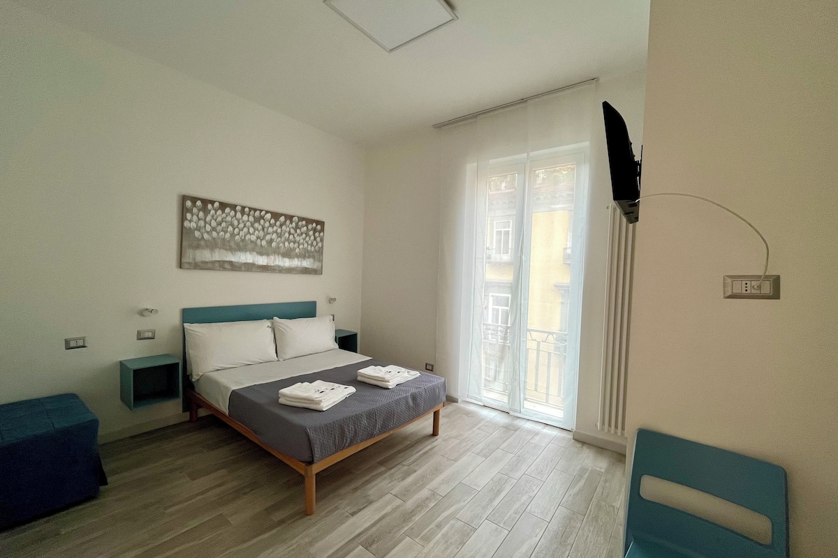 A bedroom with a bed, bedside tables, a wall-mounted TV, and a window with curtains.