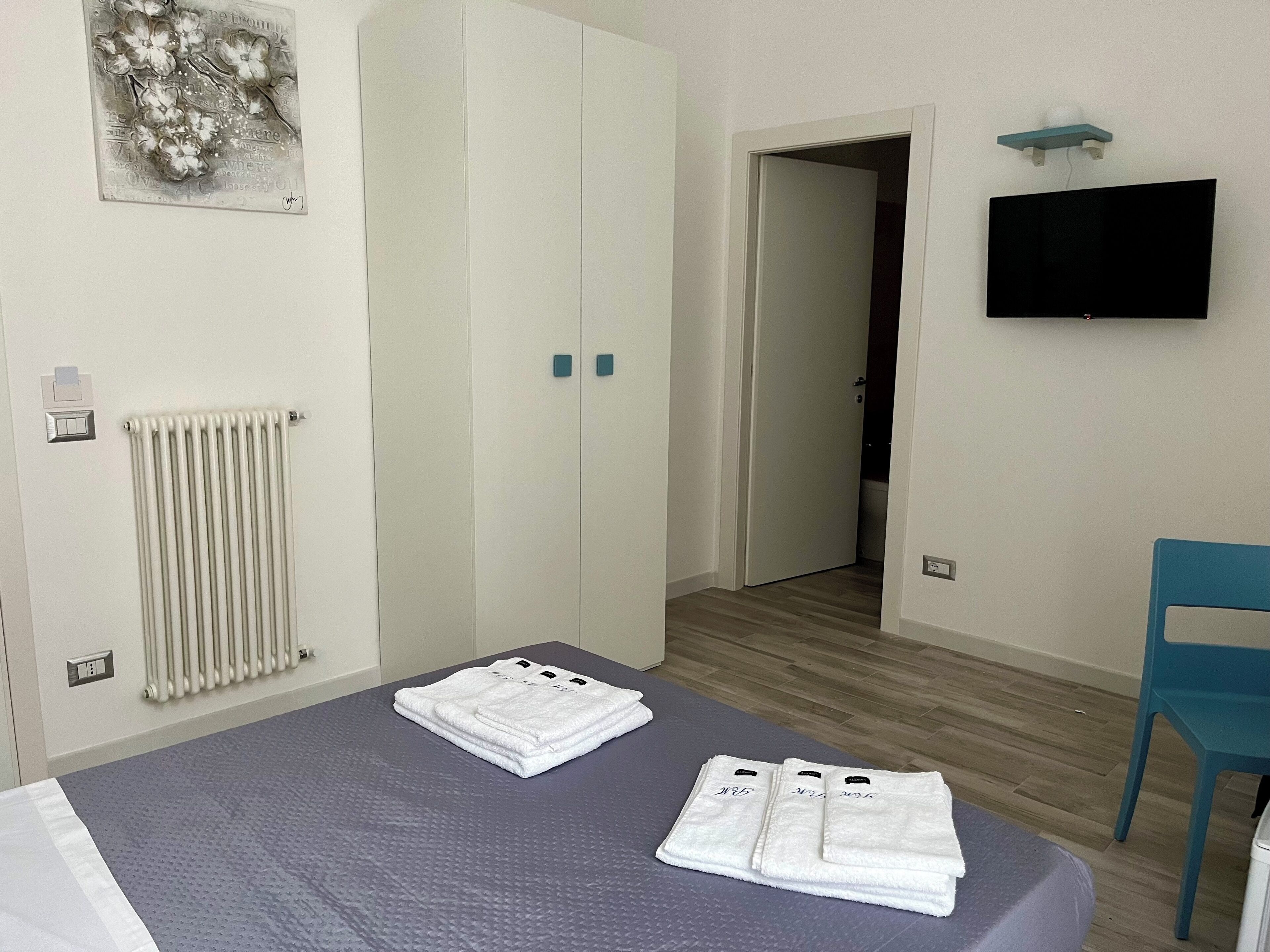 A bedroom with a bed, a radiator, a wardrobe, a TV, and a bathroom door.