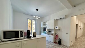 Una cocina moderna con microondas, cafetera y hervidor en la encimera. Se ve una ventana con vistas a edificios.
