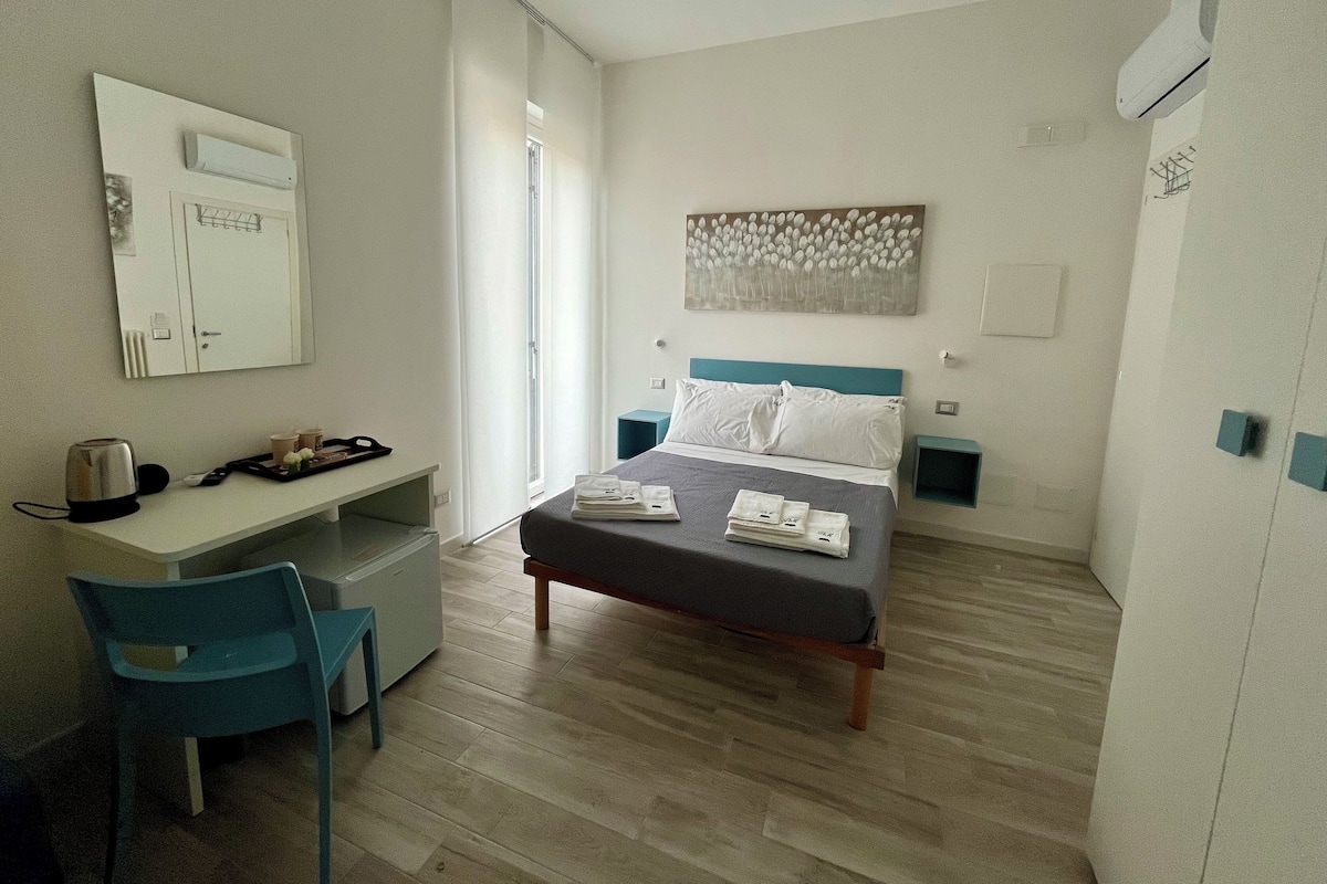 A hotel room with a bed, a desk, a chair, and a wardrobe.