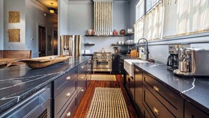 A modern kitchen with dark cabinetry, a large island, and stainless steel appliances. - Elegant Tribal House w heated Pool/Hot Tub (New Orleans)