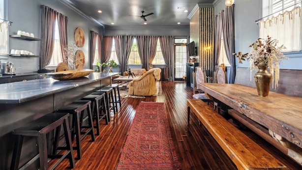 A modern kitchen with a long counter, bar stools, and a wooden bench. - Elegant Tribal House w heated Pool/Hot Tub (New Orleans)