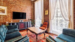 Una habitación con pared de ladrillo, televisor de pantalla plana, un armario rojo, una mesa y dos sillones azules.