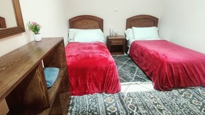 Een tweepersoonskamer met twee eenpersoonsbedden, een houten dressoir, een nachtkastje, een spiegel en een kleine potplant.
