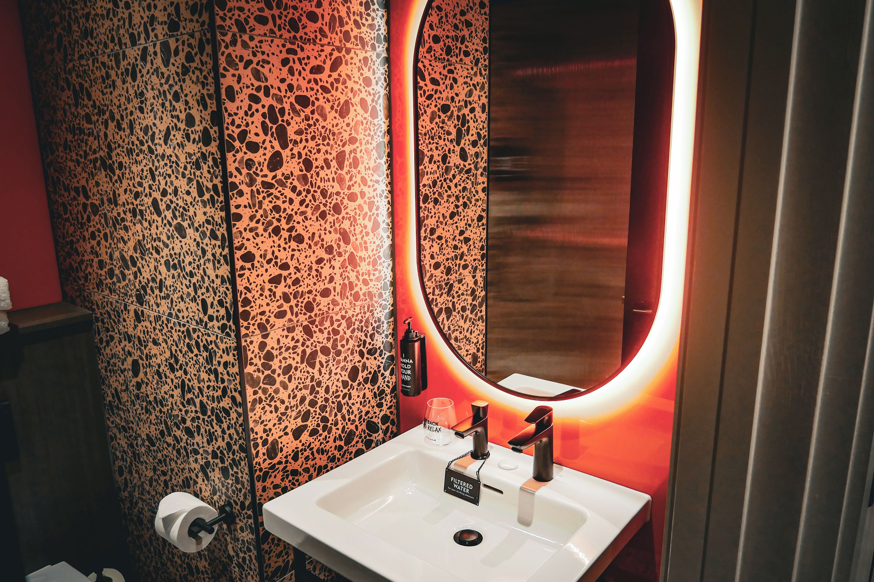 Ein Badezimmer mit einem weißen Waschbecken, einem Spiegel und einer Wand mit einem gemusterten Dekor.