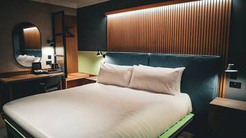 A modern hotel room with a large bed, a desk, a chair, a mirror, and a wooden panel wall.