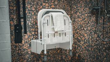 A bathroom with a white portable toilet, a black handrail, and a terrazzo floor.
