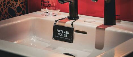 Un évier avec un panneau indiquant qu’il fournit de l’eau filtrée, un distributeur de savon et un verre sur lequel est inscrit un message.