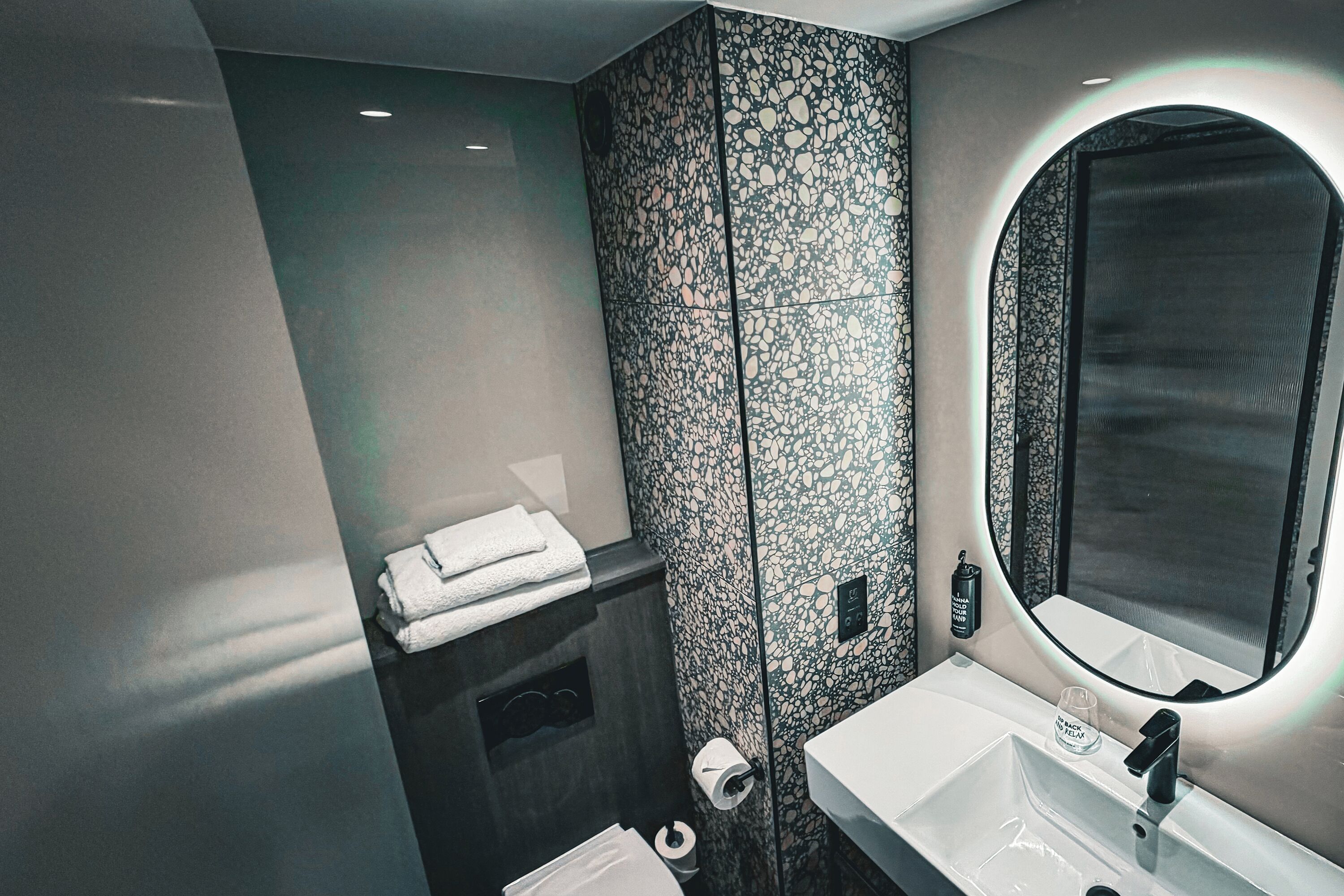 Un baño moderno con detalles de mármol, un espejo grande, un lavamanos blanco y toallas dobladas con cuidado.
