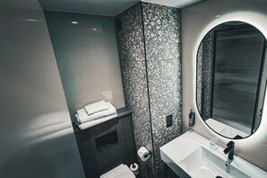 A modern bathroom with a marble backsplash, a large mirror, a white sink, and neatly folded towels. - Village Hotel Reading  (Reading)