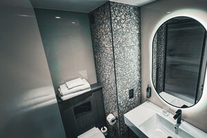 A modern bathroom with a marble backsplash, a large mirror, a white sink, and neatly folded towels.