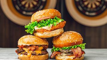 Three burgers stacked on a wooden surface with dartboards in the background.