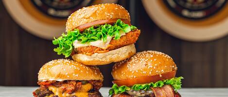 Three burgers stacked on a wooden surface with dartboards in the background.
