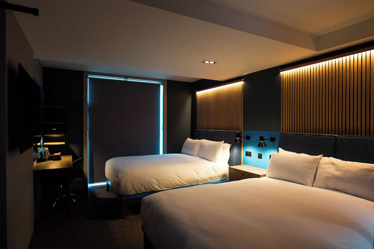 A hotel room with two beds, a desk, a chair, and a TV.