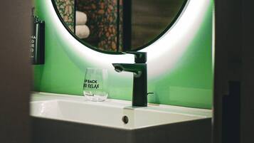 A bathroom sink with a glass reading "Sip Back and Relax" and a mirror with a circular light.