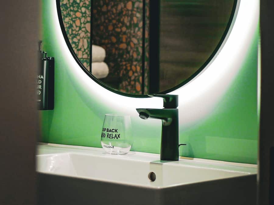 Un lavamanos con un vaso que dice 'Sip Back and Relax' y un espejo con luz circular.