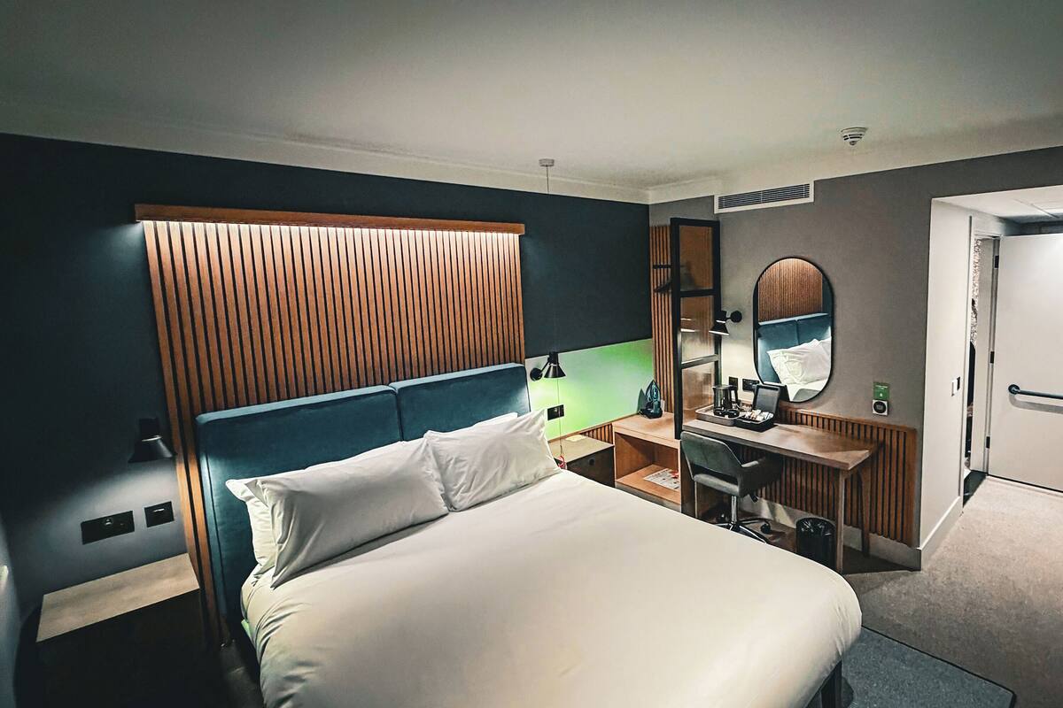A hotel room with a bed, desk, and a mirror.