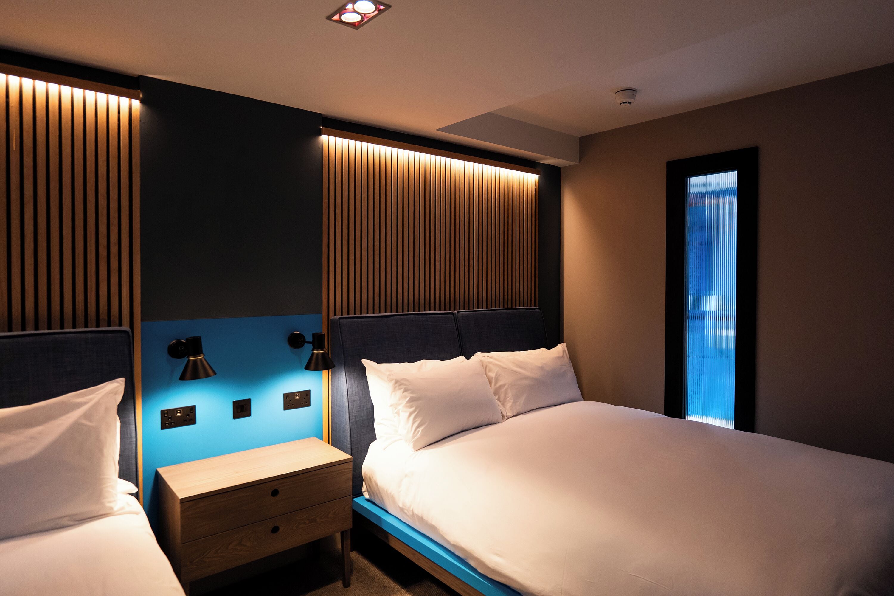 Una camera d'albergo con un letto, comodini, una lampada a parete e una finestra.