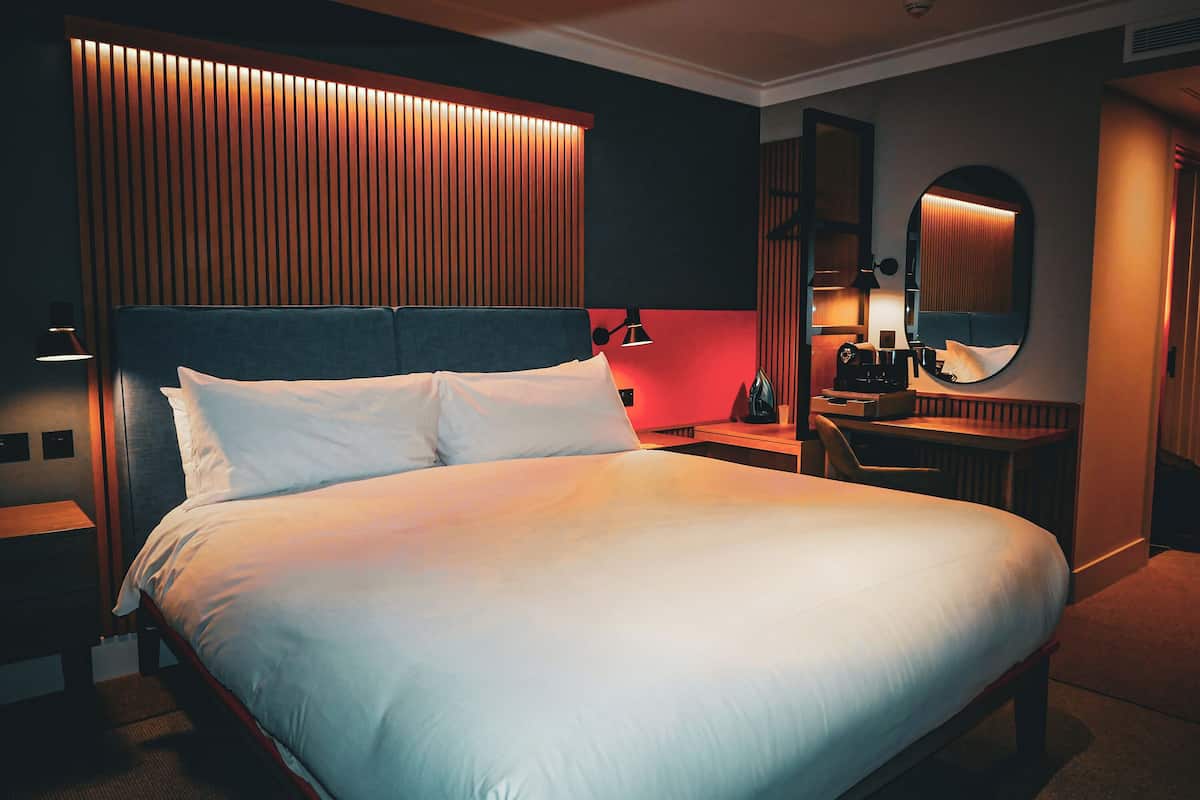 A hotel room with a large bed, bedside tables, a desk, and a mirror.