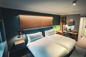 Une chambre d’hôtel avec un grand lit, des tables de chevet, un bureau avec une chaise, un miroir et une tête de lit en bois.