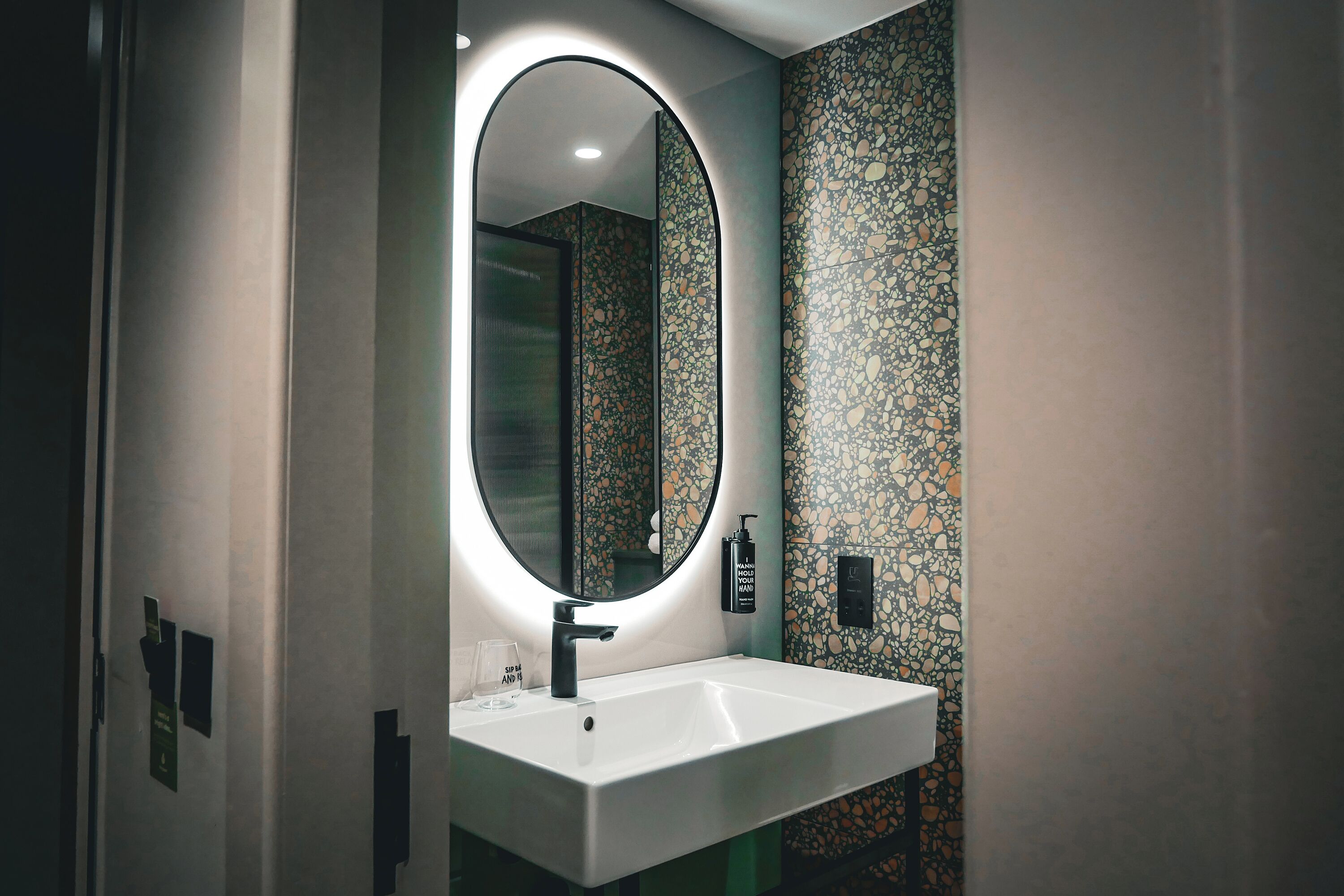 A modern bathroom with a white sink, a round mirror, and a textured wall.