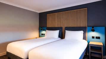 Habitación de hotel con dos camas, cabecero de madera, lámparas de noche y una mesita.