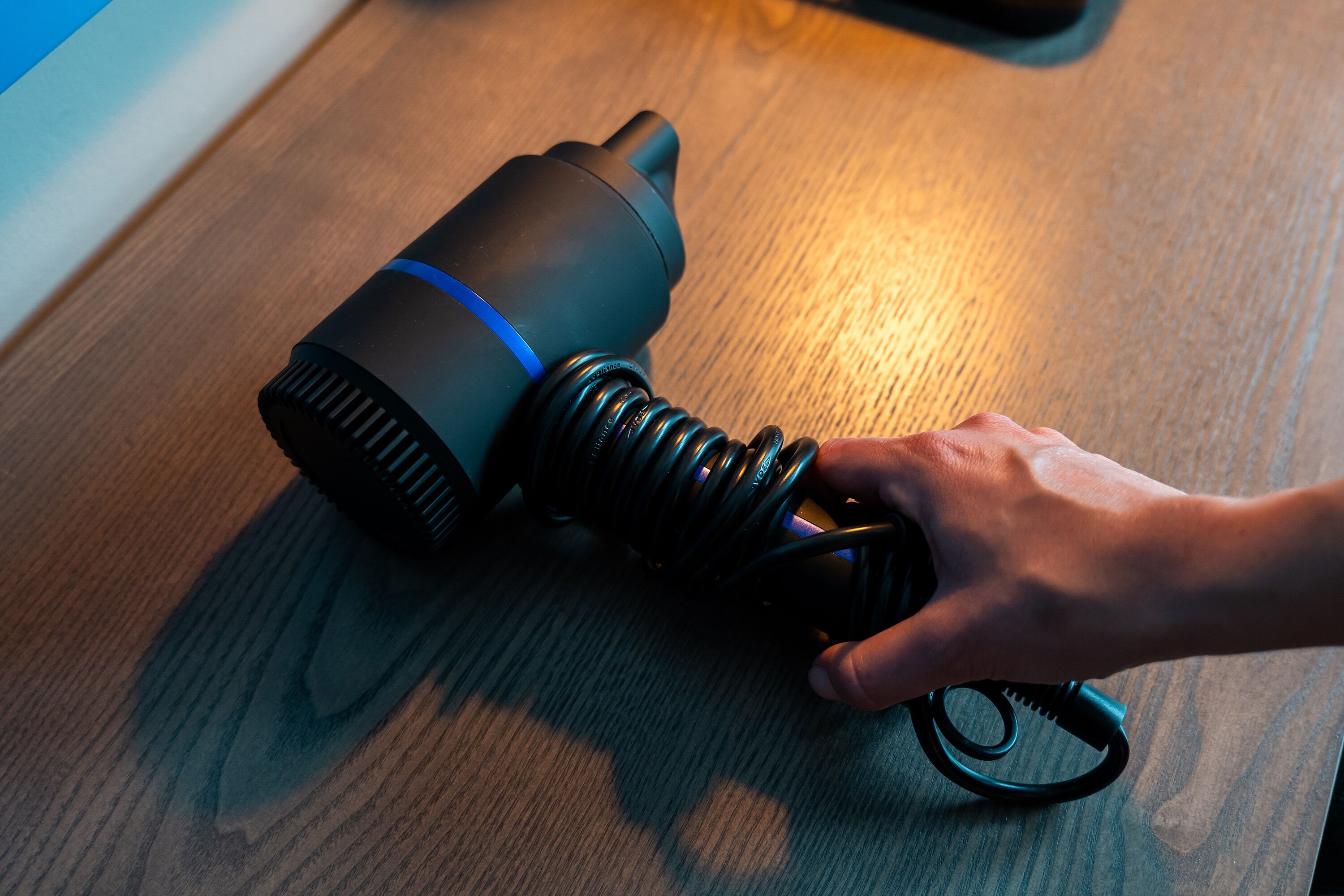 A hand adjusting a black coiled cable on a wooden surface.