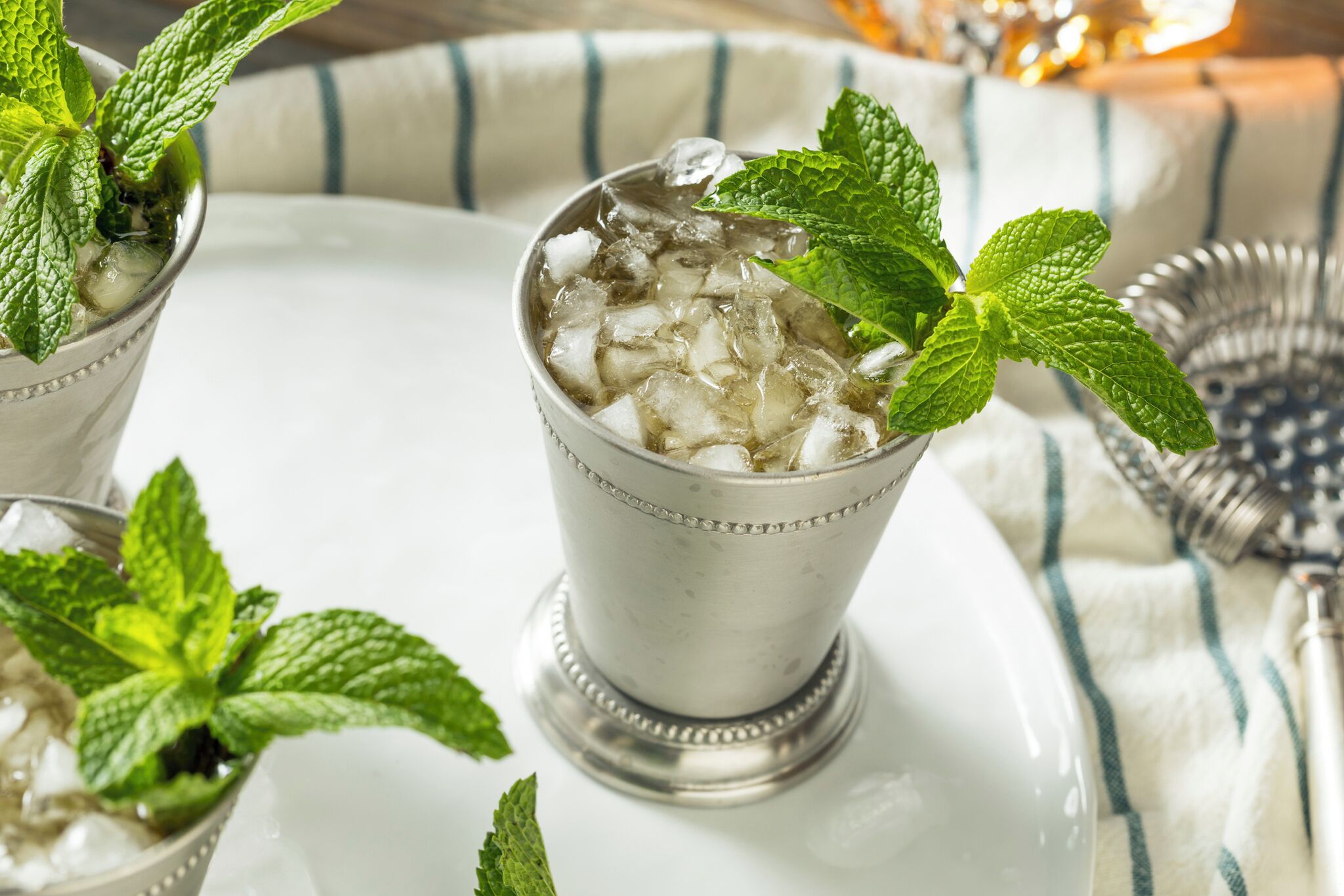 A glass with ice and mint leaves on a white tray.