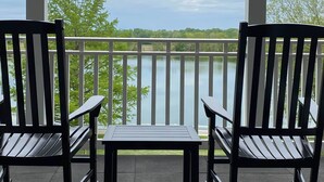 Ein Balkon mit zwei Schaukelstühlen und einem kleinen Tisch, mit Blick auf ein Gewässer und Bäume.