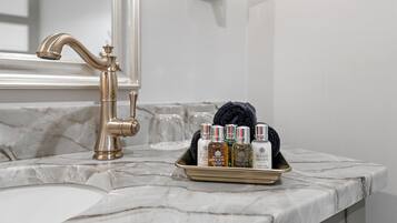 A bathroom with a marble countertop, a gold faucet, and a tray with toiletries including bottles and a towel.