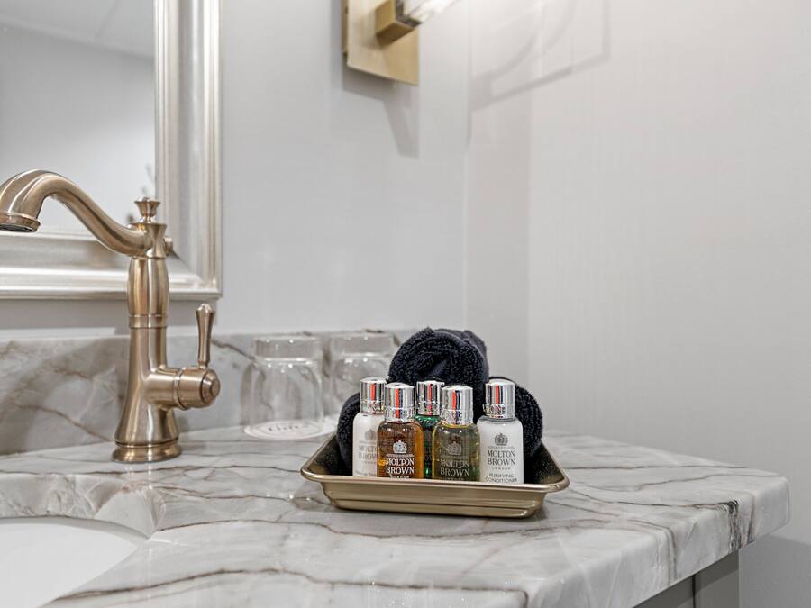 A bathroom with a marble countertop, a gold faucet, and a tray with toiletries including bottles and a towel.